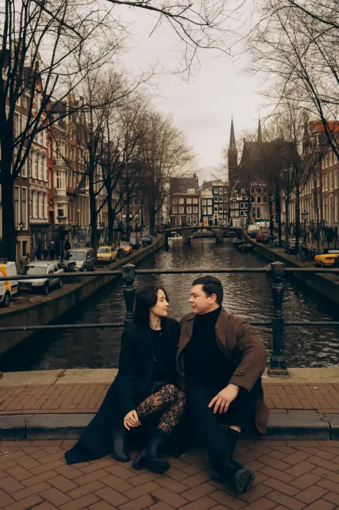 Couple sitting on a bridge above a long Amsterdam canal