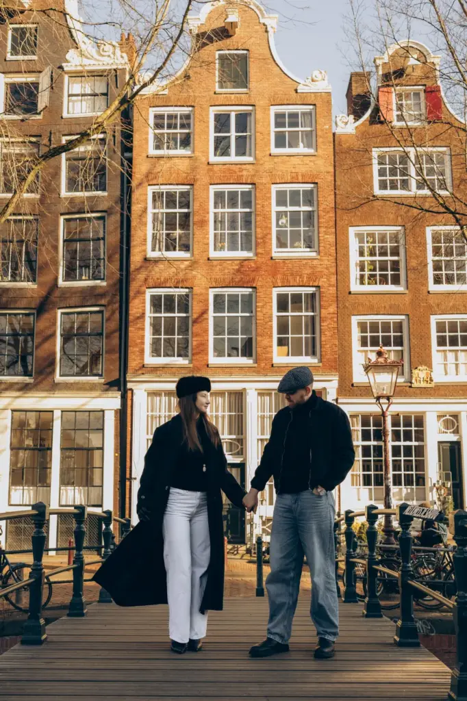 Couple walking on a canal bridge in front of gabled houses in Amsterdam